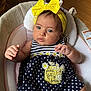 baby, child, blue_eyes, yellow_bow, headband, polka_dot_dress, daisy_embroidery, pocket, cushioned_seat, infant, clothing, cute, adorable, portrait, indoor, soft_lighting, person, small_hands, curious_expression, fabric