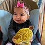 baby, baby_chair, child, clothing, cute, face, hands, happy, headband, indoor, infant, patterned_pants, person, pink_bow, playful, plush_toy, seated, smiling, toy, yellow_toy