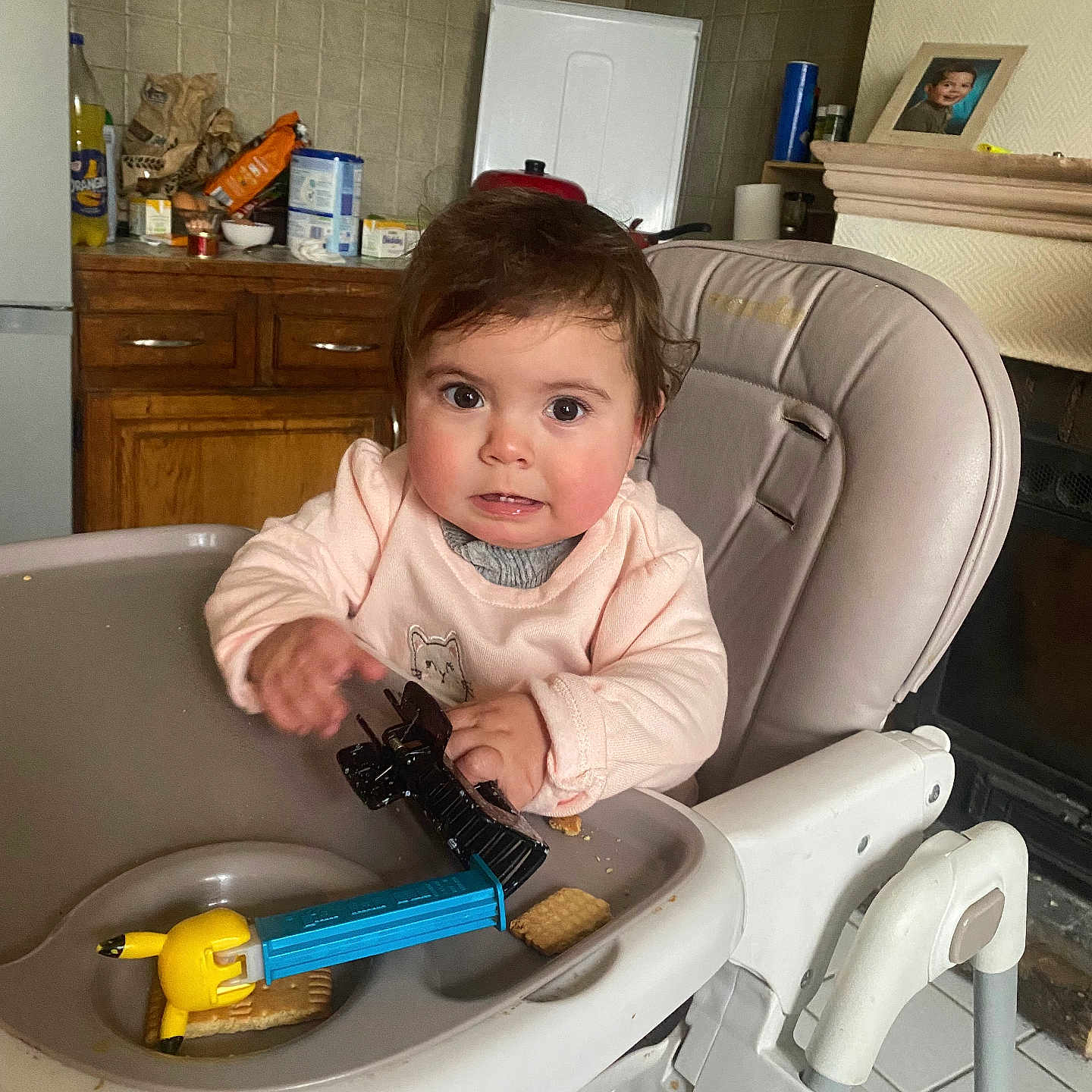 Anaïa a rejoint le concours — aidez-le/la à gagner de superbes lots ! baby, brown_hair, cabinet, child, clothing, cracker, crumbs, expression, face, framed_photo, hair_clip, highchair, indoor, kitchen, plastic_toy, portrait, snack, toddler, toy, tray