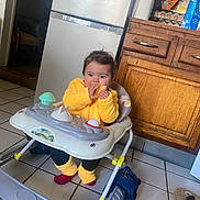 Anaïa a rejoint le concours — aidez-le/la à gagner de superbes lots ! baby, child, walker, kitchen, refrigerator, wooden_cabinet, tile_floor, toy, snack, eating, yellow_jacket, socks, red_socks, seat, cute, portrait, indoor, appliance, backpack, slipper