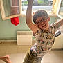 boy, car, casual_clothing, child, daylight, floor, glasses, happy, home, indoor, jumping, light, motion, person, playful, remote, shorts, smiling, tshirt, window