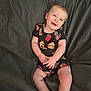baby, child, smiling, infant, clothing, black_onesie, fast_food_pattern, pizza, burger, fries, soda_can, couch, fabric, comfortable, happy, portrait, sitting, cute, skin, hands