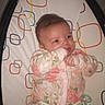 baby, infant, onesie, floral, baby_seat, patterned, hand_in_mouth, cute, comfort, indoor, child, face, expression, sitting, soft_lighting, young, small_hands, pacifier, colorful, fabric