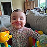 Kennedy is registered to the contest to win money with this photo: activity_center, baby, baby_toys, chandelier, child, colorful_toys, couch, floral_clothing, happy, home, indoor, infant, kitchen, living_room, playtime, portrait, sitting, smiling, window, wooden_cabinet