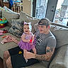 baby, child, father, family, smiling, happy, purple_dress, tutu, hair_bow, toy, red_toy, couch, living_room, indoor, dog, patio, window, door, tattoo, portrait
