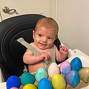 Ashton is registered to the contest to win money with this photo: baby, child, colorful, door, easter_eggs, face, hands, happy, high_chair, indoor, infant, looking_sideways, plastic_tray, playful, seat_belt, skin, smiling, table, wall, white_wall
