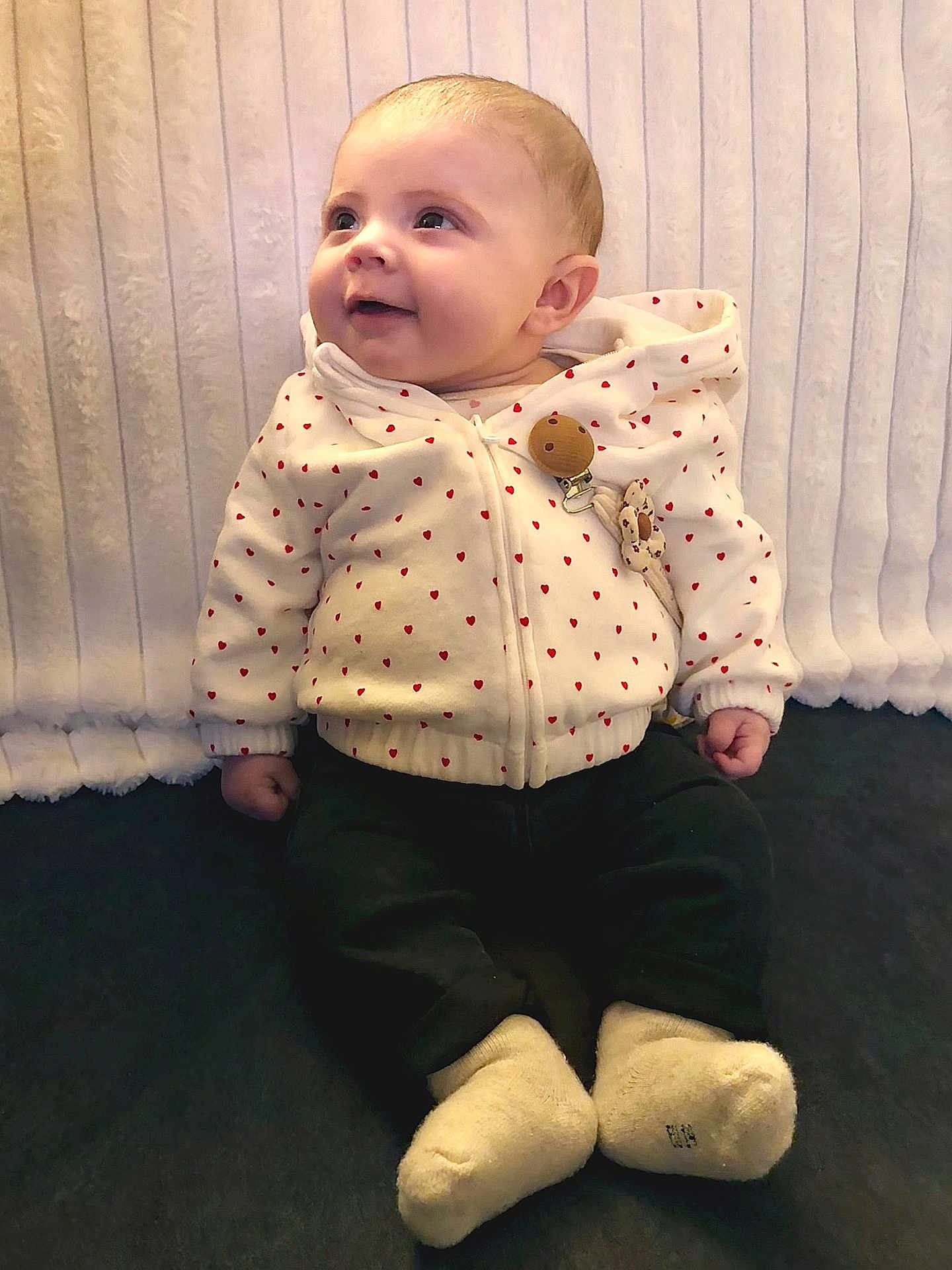 Romy a rejoint le concours — aidez-le/la à gagner de superbes lots ! baby, child, hoodie, white_clothing, red_hearts, sitting, smiling, happy, face, infant, cute, cozy, warm_clothing, socks, indoor, portrait, young_child, looking_up, soft_background, casual