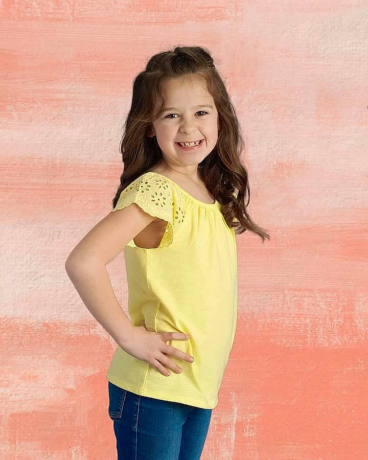 Alayna is registered to the contest to win money with this photo: arm, blouse, child, child_model, clothing, gesture, joy, neck, person, photo_shoot, photography, shoulder, sleeve, smile, standing, t_shirt, toddler, top, yellow