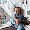 Everett is registered to the contest to win money with this photo: baby, child, infant, smiling, sitting, couch, blanket, pillow, clothing, blue_outfit, portrait, indoor, home, furniture, textile, numbered_blanket, quilt, colorful, happy, facial_expression