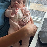 Julianna is registered to the contest to win money with this photo: baby, sleeping, infant, pink_onesie, headband, adult_hand, window, natural_light, indoor, person, child, seated, peaceful, closeup, portrait, soft_fabric, floral_pattern, skin, fingers, face