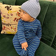 Abraham joined the competition — help win amazing prizes! baby, child, blue_onesie, knit_hat, striped_clothing, green_couch, pillow, embroidery, indoor, furniture, cute, infant, sitting, hand, foot, curious, face, portrait, soft_texture, cozy