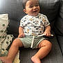 baby, smiling, child, mickey_mouse, tshirt, shorts, couch, pillow, blanket, indoor, happy, cute, person, infant, home, comfort, seated, drawstring, foot, face