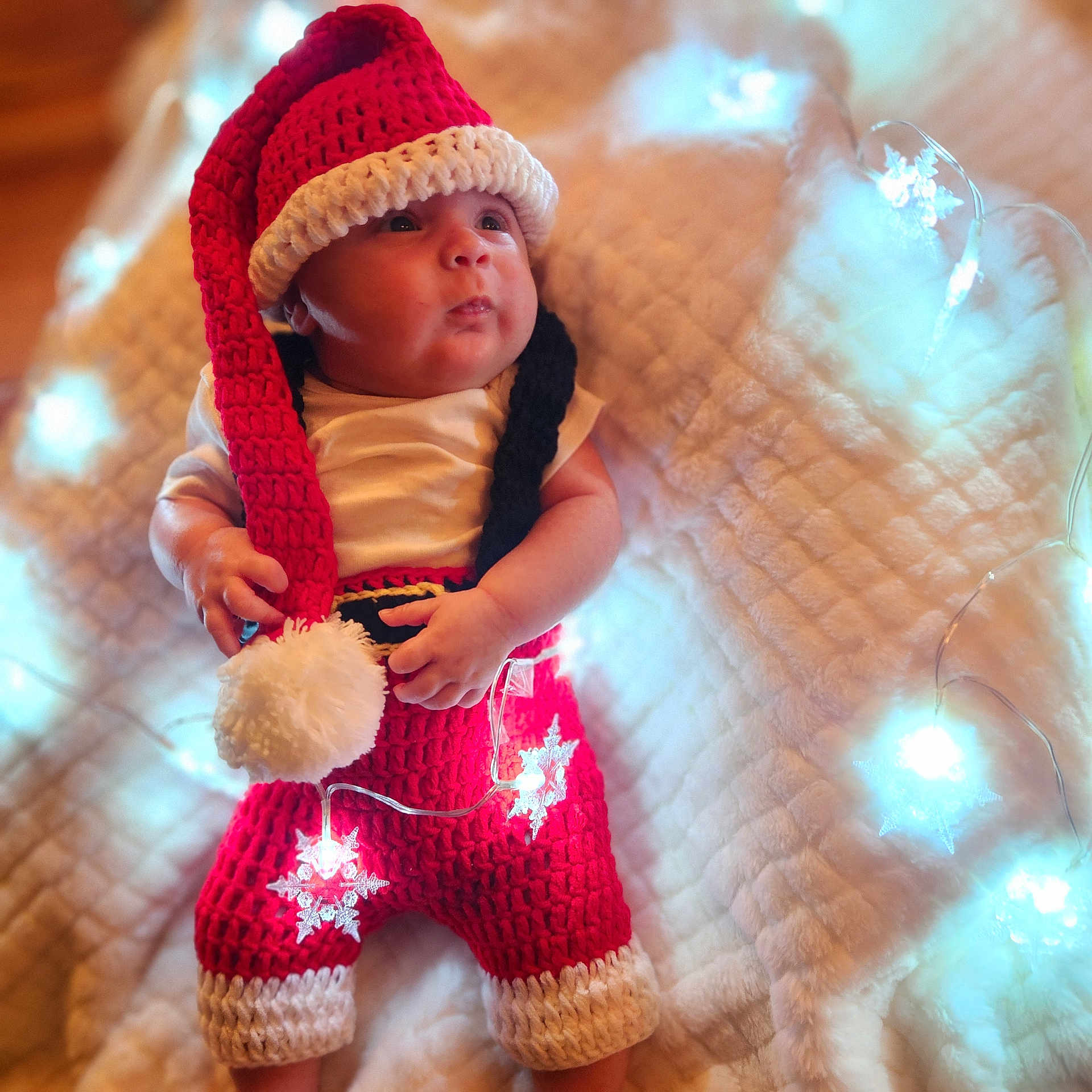 J'Ansel joined the competition — help win amazing prizes! baby, blanket, child, christmas, cozy, cute, fairy_lights, festive, holiday_theme, indoors, infant, knitted_clothing, newborn, portrait, red_outfit, santa_hat, smiling, snowflake_lights, soft_texture, white_pom_pom