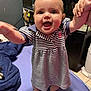 Layla is registered to the contest to win money with this photo: baby, bed, blanket, child, clothing, cute, eyes, face, feet, furniture, hand_holding, happy, home, indoor, infant, person, portrait, smiling, striped_dress, support