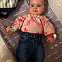 baby, infant, child, crib, mattress, clothing, pink_top, denim_jeans, face, eyes, hands, feet, pattern, arrows, bows, cute, smiling, indoor, soft_lighting, comfortable