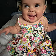 Layla is registered to the contest to win money with this photo: baby, blanket, cartoon_print, child, colorful, cute, dress, expression, eyes, face, hair, hands, happy, indoors, person, portrait, sitting, skin, smiling, soft_toys