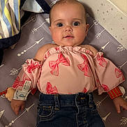 Layla is registered to the contest to win money with this photo: baby, child, infant, face, clothing, pink_top, denim_jeans, blanket, mattress, pattern, arrow_pattern, striped_blanket, cute, wide_eyes, lying_down, indoor, soft_lighting, adorable, person, portrait