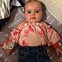 baby, child, infant, face, clothing, pink_top, denim_jeans, blanket, mattress, pattern, arrow_pattern, striped_blanket, cute, wide_eyes, lying_down, indoor, soft_lighting, adorable, person, portrait