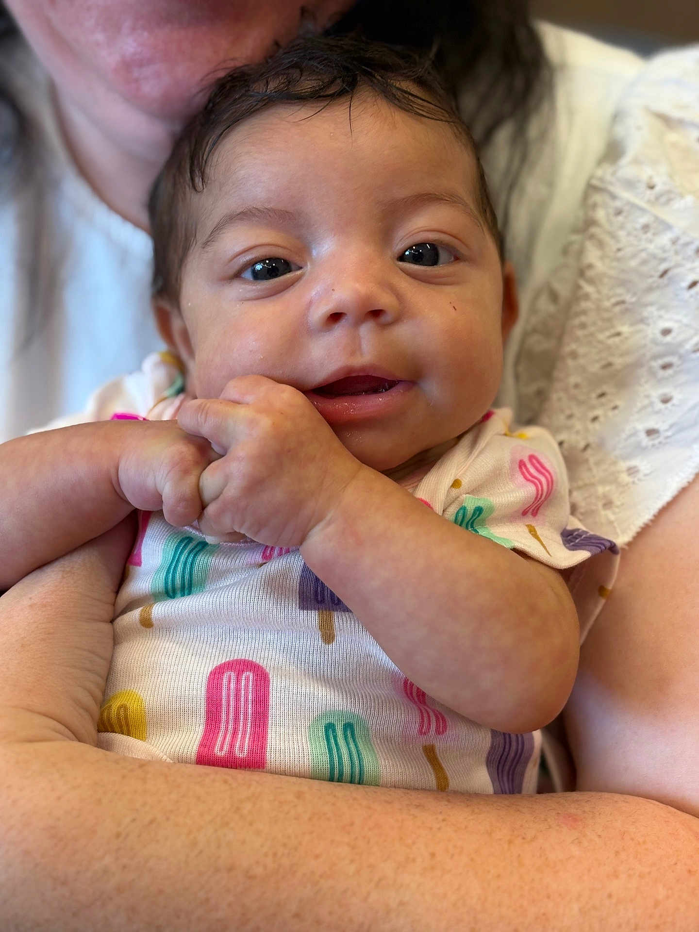 Alani is registered to the contest to win money with this photo: baby, infant, child, person, holding, arms, close_up, cute, smiling, onesie, colorful_clothing, popsicle_pattern, skin, face, eyes, hands, adult, love, comfort, family