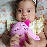 Alice is registered to the contest to win money with this photo: baby, child, plush_toy, pink, bow, headband, cushion, rainbow, stars, yellow_dress, indoor, closeup, smiling, cute, infant, soft_toy, hands, face, happy, portrait