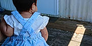 Alice joined the competition — help win amazing prizes! baby, child, back_view, blue_dress, ponytail, outdoor, wooden_porch, person_holding, summer_clothing, sunlight, wooden_floor, door, screen_door, casual, cute, infant, holding, daylight, patterned_clothing, small_hair_tie