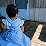 baby, child, back_view, blue_dress, ponytail, outdoor, wooden_porch, person_holding, summer_clothing, sunlight, wooden_floor, door, screen_door, casual, cute, infant, holding, daylight, patterned_clothing, small_hair_tie