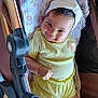 baby, child, smiling, yellow_outfit, headband, stroller, blanket, infant, cute, happy, face, person, clothing, fabric, skin, arm, leg, indoors, portrait, resting