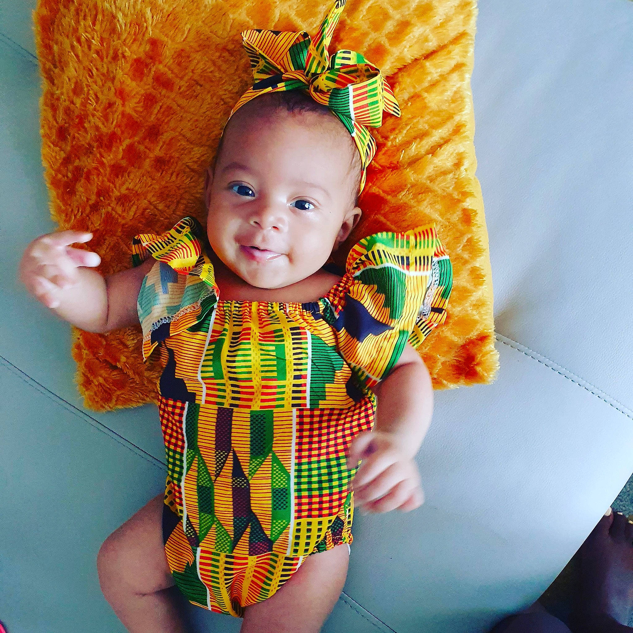 Myla participe au concours pour gagner de l'argent avec cette photo : baby, baby_products, baby_toddler_clothing, child, clothing, crochet, green, headgear, orange, pattern, person, sleeve, textile, toddler, yellow