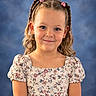 Mila joined the competition — help win amazing prizes! child, girl, portrait, smiling, floral_dress, braids, hair_clips, pink_flowers, blue_background, studio, headshot, standing, young_person, face, eyes, earrings, fashion, formal_pose, photography, indoor