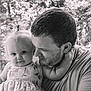 baby, child, man, outdoor, forest, black_and_white, portrait, tender_moment, person, nature, smile, face, hair, clothing, holding, parent, affection, cute, young_child, family