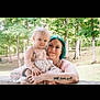 woman, child, toddler, outdoor, trees, greenery, park, holding, smiling, portrait, casual, floral_dress, tattoos, family, nature, happy, daylight, cute, affection, love