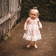Khaleesi is registered to the contest to win money with this photo: toddler, child, barefoot, floral_dress, outdoor, curious, standing, concrete, wooden_fence, greenery, ponytail, portrait, daylight, nature, young_child, cute, innocent, summer, casual, person