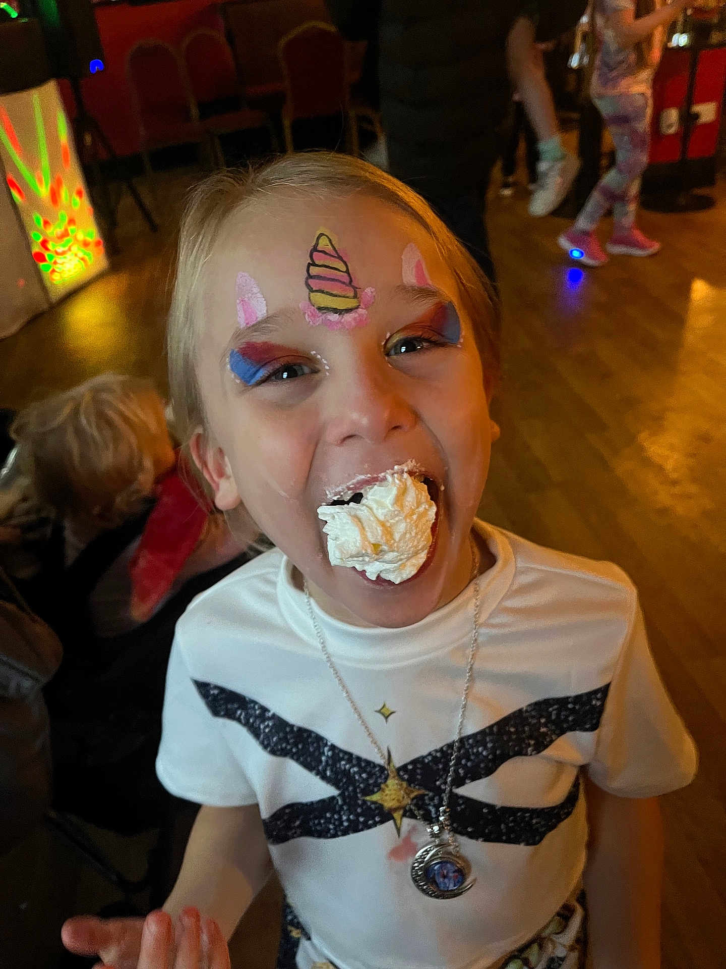 Melody-Kay joined the competition — help win amazing prizes! child, face_paint, unicorn, whipped_cream, party, happy, smiling, fun, indoor, celebration, tshirt, necklace, food, messy, people, floor, background, colorful, event, joy