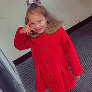 Aurora-May is registered to the contest to win money with this photo: child, girl, red_coat, smiling, indoor, carpet, wall, bow, hair_accessory, playful, posing, footwear, pants, buttoned_coat, happy, person, young, cute, fashion, casual