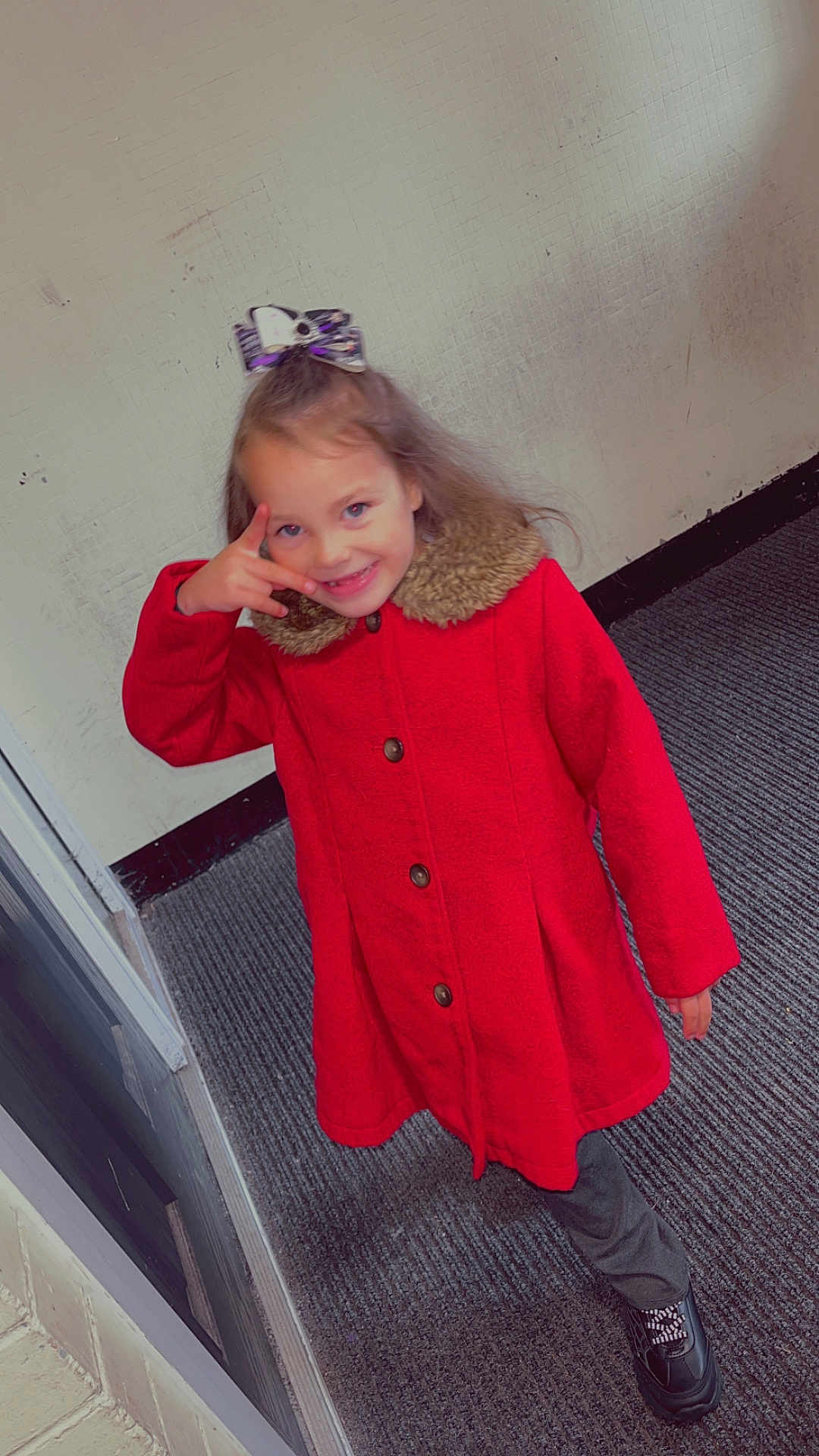 Aurora-May is registered to the contest to win money with this photo: child, girl, red_coat, smiling, indoor, carpet, wall, bow, hair_accessory, playful, posing, footwear, pants, buttoned_coat, happy, person, young, cute, fashion, casual
