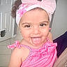 child, toddler, girl, smiling, tongue_out, headband, bow, curly_hair, pink_clothing, striped_dress, indoors, tile_floor, door, playful, cute, happy, portrait, person, baby, expression