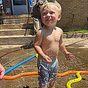 Cameron joined the competition — help win amazing prizes! toddler, child, water, sprinkler, summer, barefoot, play, outdoor, sunlight, brick_wall, concrete, hose, water_droplets, happy, smiling, shorts, people, adult, family, backyard