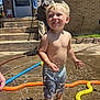 toddler, child, water, sprinkler, summer, barefoot, play, outdoor, sunlight, brick_wall, concrete, hose, water_droplets, happy, smiling, shorts, people, adult, family, backyard