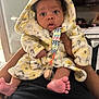 baby, infant, hooded_robe, pacifier, colorful_clip, bare_feet, hands, adult, indoor, living_room, television, furniture, person, cute, soft_texture, warm_clothing, close_up, portrait, expression, holding