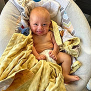 Luca is registered to the contest to win money with this photo: baby, smiling, blanket, pacifier, infant, diaper, baby_seat, happy, cute, child, skin, furniture, indoors, cozy, toddler, soft, wrapped, playful, relaxed, comfort