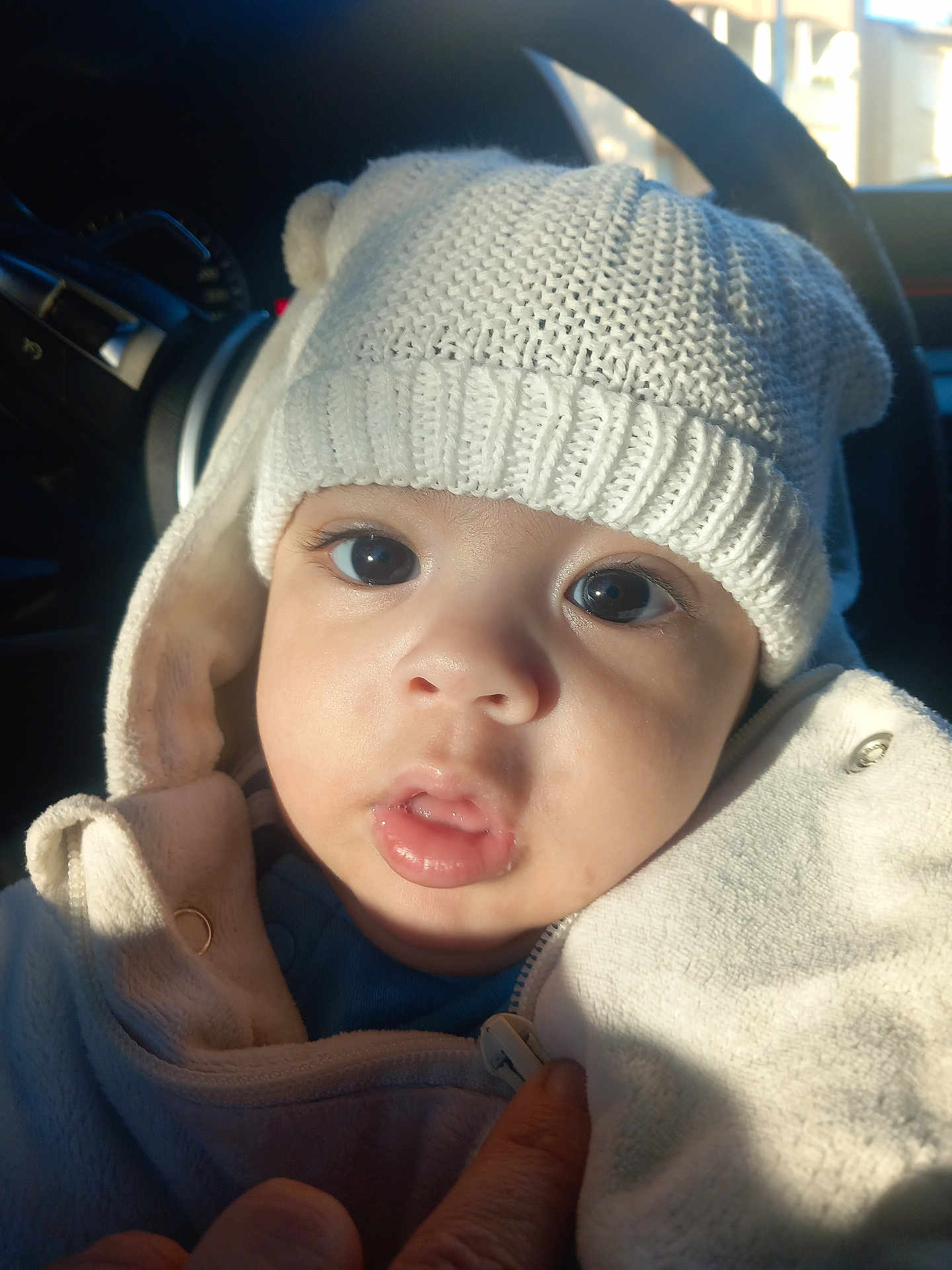 Kalïl a rejoint le concours — aidez-le/la à gagner de superbes lots ! baby, child, hat, knitted_hat, white_clothing, jacket, face, eyes, mouth, hand, car_interior, sunlight, portrait, closeup, cute, warm_light, winter_clothing, infant, cozy, expression