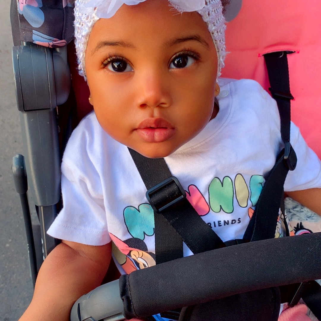 Kayanah a rejoint le concours — aidez-le/la à gagner de superbes lots ! baby, child, clothing, curious, cute, eyes, face, flower, headband, infant, outdoor, person, pink_pants, portrait, shirt, sitting, straps, stroller, toddler, white