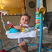 Esmail is registered to the contest to win money with this photo: baby, infant, child, face, person, sitting, activity_center, jumper, baby_toy, toy_car, colorful, indoor, living_room, carpet, furniture, chair, home, portrait, curious, playtime