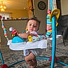 baby, infant, child, face, person, sitting, activity_center, jumper, baby_toy, toy_car, colorful, indoor, living_room, carpet, furniture, chair, home, portrait, curious, playtime
