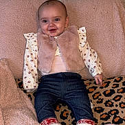Elsie joined the competition — help win amazing prizes! baby, child, smiling, indoor, blanket, fur_vest, boots, jeans, patterned_shirt, leopard_print, cushion, cozy, soft_texture, happy, portrait, clothing, person, infant, cute, warm