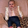 baby, child, smiling, indoor, blanket, fur_vest, boots, jeans, patterned_shirt, leopard_print, cushion, cozy, soft_texture, happy, portrait, clothing, person, infant, cute, warm