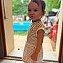 toddler, child, striped_dress, pink_shoes, doorway, backyard, kiddie_pool, blurred_background, curious, standing, short_hair, earrings, outdoor, daylight, person, portrait, cute, young_child, summer, home