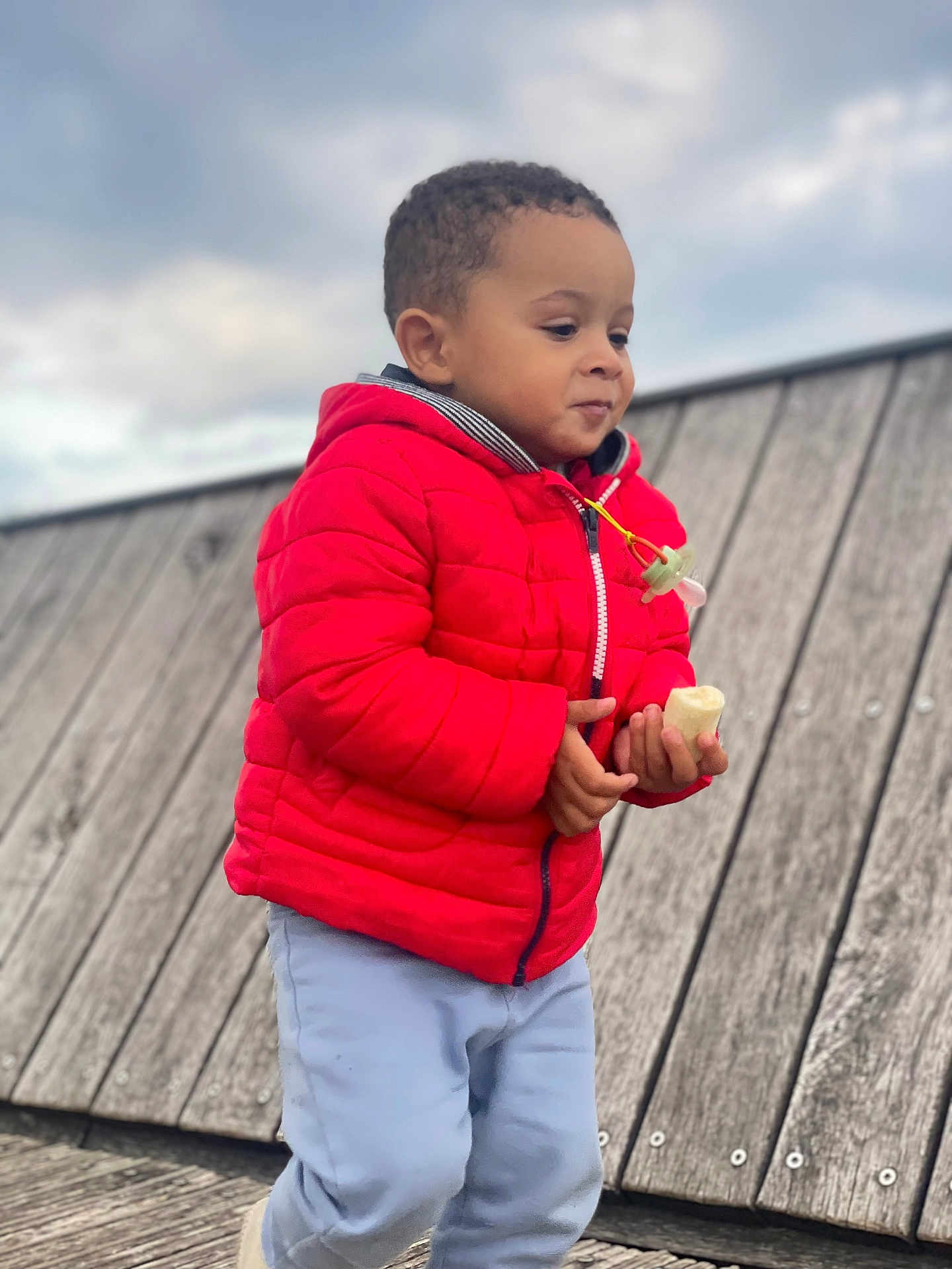 Noah Daniel participe au concours pour gagner de l'argent avec cette photo : child, kid, red_jacket, banana, food, outdoor, wood, cloudy_sky, pants, cute, portrait, person, walking, holding, young_child, casual_clothing, daytime, expression, curly_hair, nature