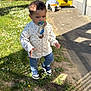 background_child, blue_pants, child, curly_hair, daylight, flowers, grass, nature, outdoor, pacifier, person, playground, polka_dot_jacket, serious_expression, shadow, sidewalk, sneakers, sunny, toddler, toy_vehicle