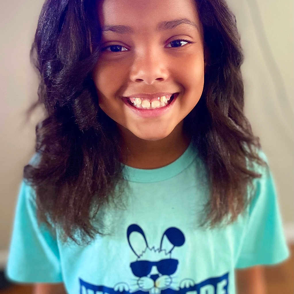 Hailey is registered to the contest to win money with this photo: bodypart, child, clothing, dimples, face, female, girl, hair, happy, head, mouth, person, photography, portrait, purple, shirt, sleeve, smile, t_shirt, teeth